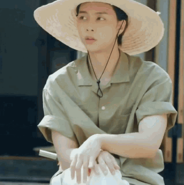 a man wearing a straw hat is sitting down with his hands folded