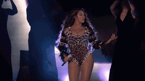 a woman in a bodysuit is holding a microphone on a stage