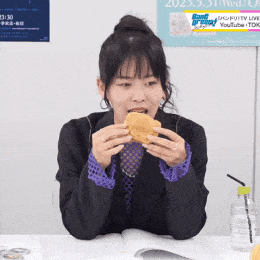 a woman eating a sandwich in front of a sign that says ' ban dream ' on it