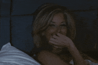 a woman covering her mouth with her hand while lying on a bed