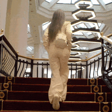 a woman is walking up a set of stairs with a chandelier in the background