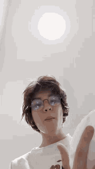 a young man wearing glasses and a white shirt is holding a cell phone in his hand .