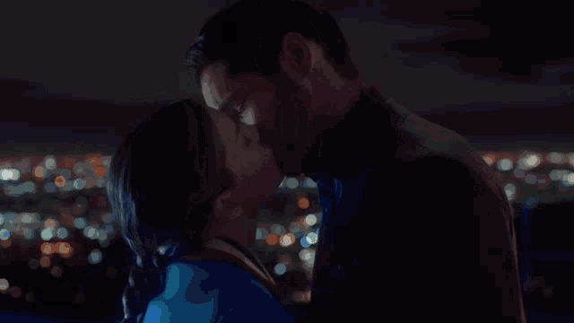 a man and a woman are kissing in front of a city skyline