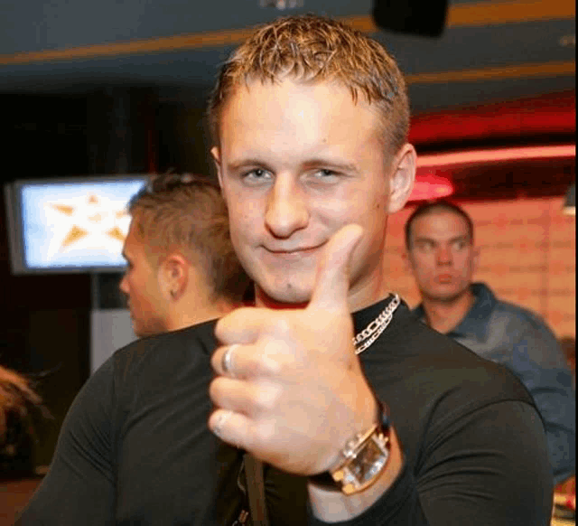 a man in a black shirt is giving a thumbs up and has a watch on his wrist