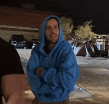 a man in a blue hoodie is standing in a parking lot .