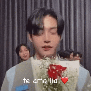 a man is holding a bouquet of flowers in front of his face and saying `` te amo lia '' .