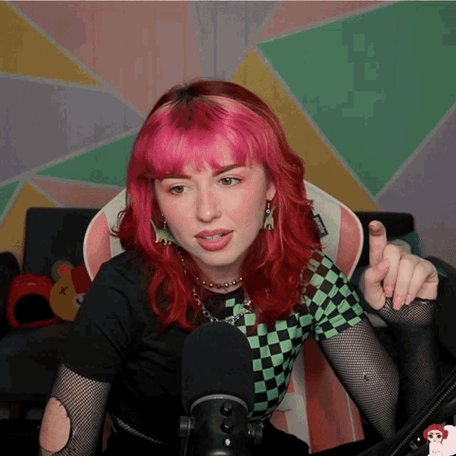 a woman with pink hair is sitting in front of a microphone and giving a thumbs up