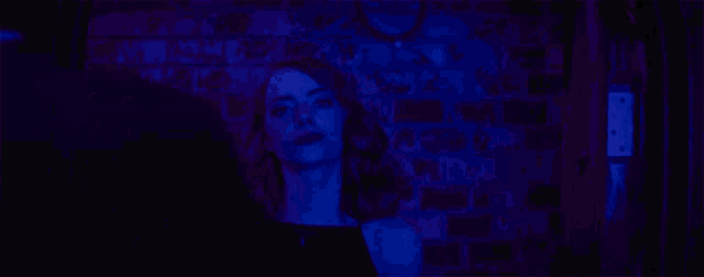 a woman is standing in front of a brick wall in a dark room with blue lights .