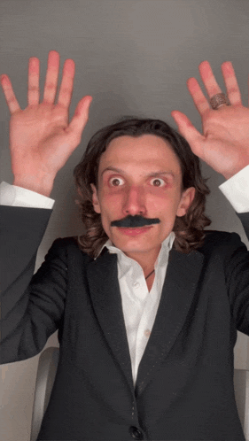 a man in a suit with a fake mustache holds his hands up