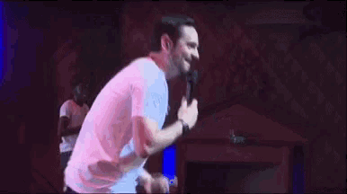 a man in a white t-shirt is holding a microphone and dancing on a stage .