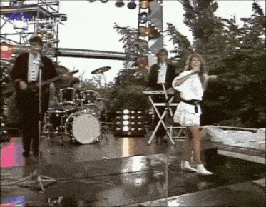 a woman singing into a microphone on a stage with a band in the background