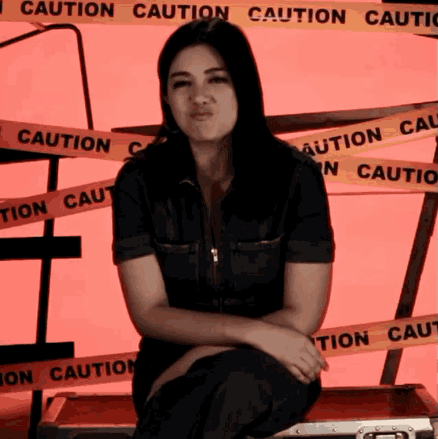a woman is sitting in front of a caution tape wall