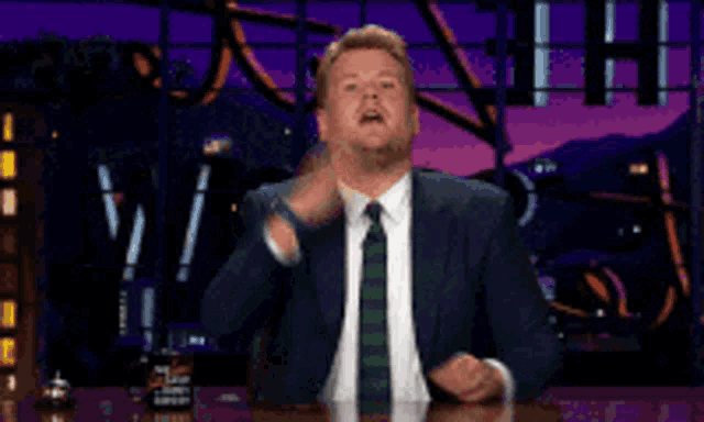 a man in a suit and tie is sitting at a table making a funny face