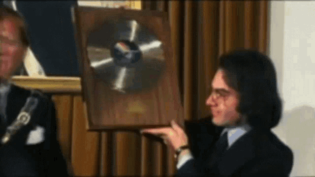 a man in a suit is holding a wooden plaque with a gold record on it