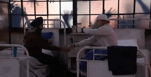 a man in a turban is sitting in a hospital bed talking to another man