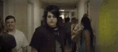 a group of people are walking down a hallway with a man wearing a mask .