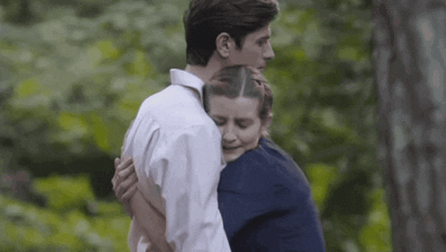 a man and a woman hugging each other in a forest