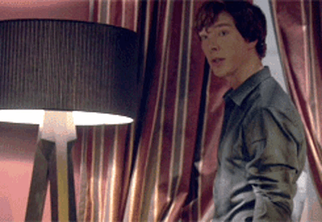 a man standing in front of a lamp with a striped curtain behind him