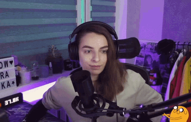 a woman wearing headphones stands in front of a microphone with a sign that says 37.6k in the background