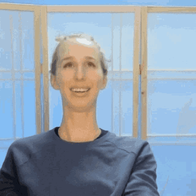 a woman wearing a blue shirt is smiling in front of a blue wall
