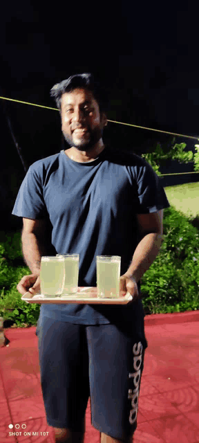 a man wearing adidas shorts is holding a tray with two glasses of liquid on it