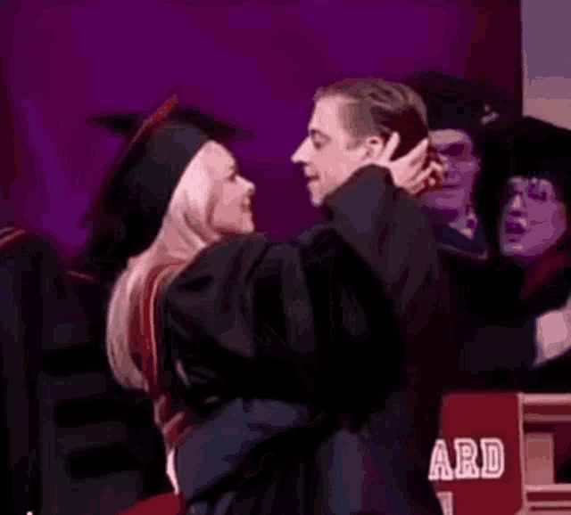 a man in a graduation cap and gown is hugging a woman in a cap and gown