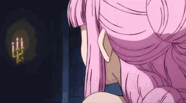 a woman with pink hair is looking at a candle in a dark room .