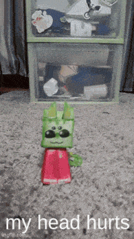 a toy cat is sitting on a carpet with the words " my head hurts " written below it