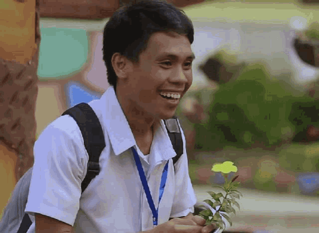 a young man with a lanyard around his neck holds a yellow flower in his hand