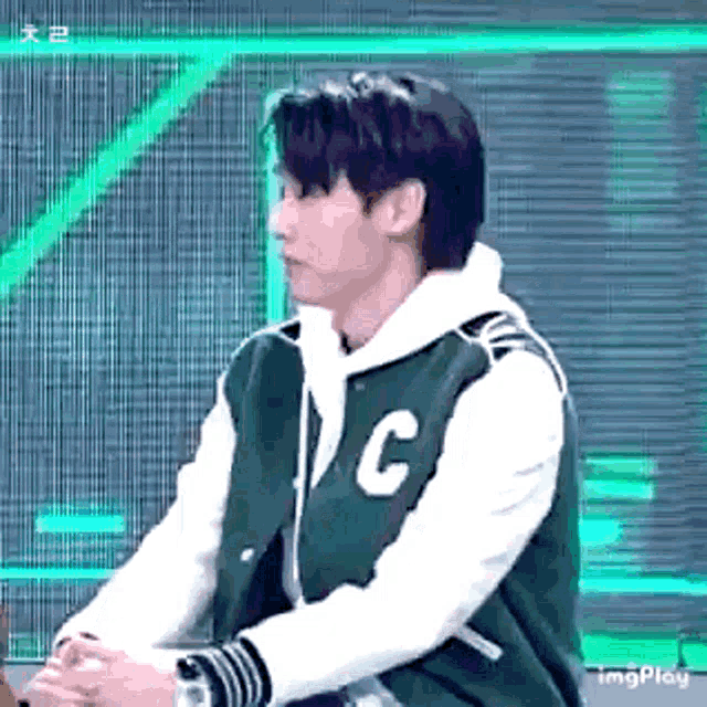 a man wearing a green varsity jacket with the letter c on it