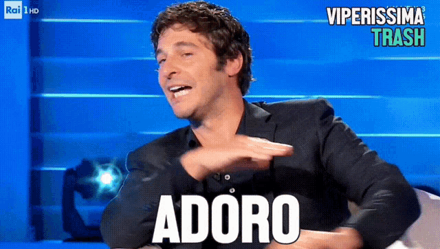 a man sitting in front of a screen that says adoro on it