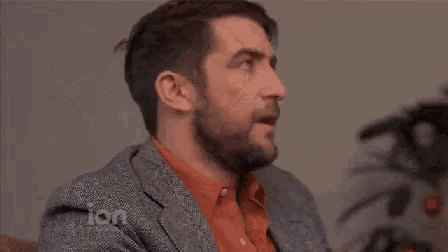 a man with a beard is sitting on a couch with his hands behind his head and the words ion television behind him