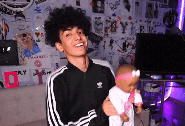 a young man in an adidas jacket holds a baby doll in his arms