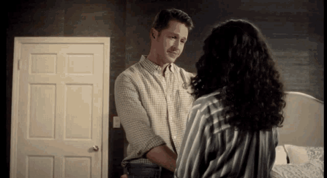 a man and woman are standing next to each other in a bedroom .