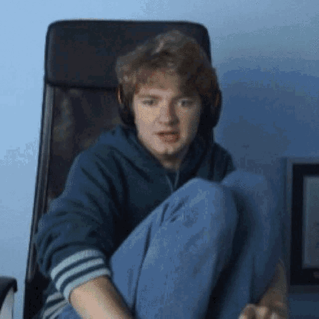 a young man is sitting in a chair with his legs crossed while wearing headphones .