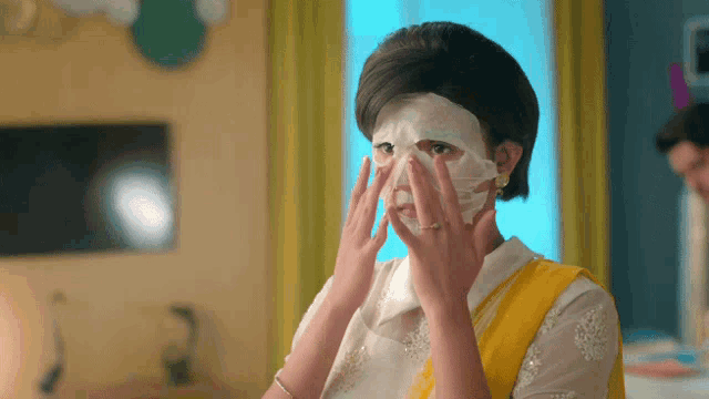 a woman in a yellow sari is applying a mask to her face