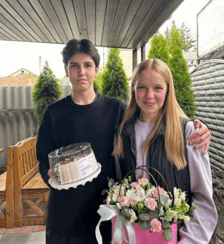 a boy and a girl are holding a cake and flowers .