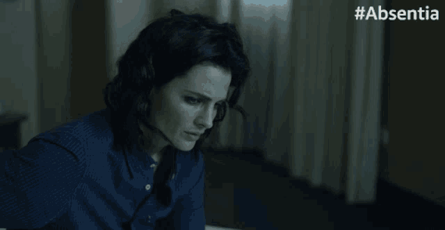 a woman in a blue shirt is crying in a dark room with #absentia written on the bottom