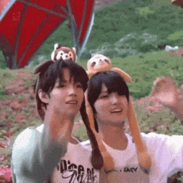 two young men wearing stuffed animals on their heads are standing next to each other in a park .