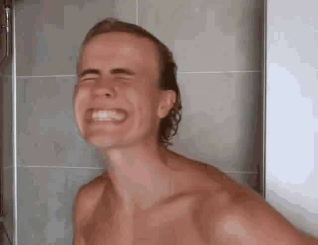 a shirtless man is laughing in a shower .