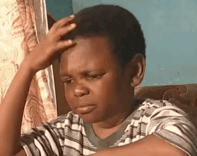 a young boy is sitting on a couch holding his head and making a funny face .