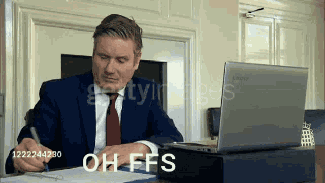 a man in a suit and tie is sitting at a desk in front of a laptop with the words oh ffs written on the screen