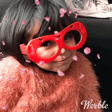 a little girl wearing red heart shaped glasses and a pink fur coat with petals falling around her