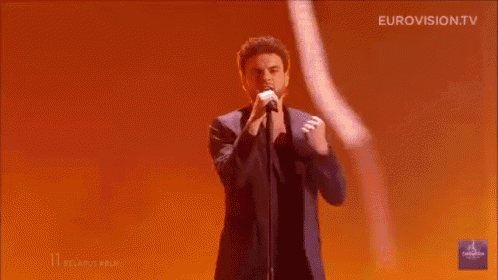 a man is singing into a microphone on a stage with his hands in the air .