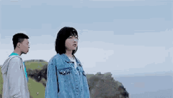 a man and a woman are standing next to each other on top of a cliff .