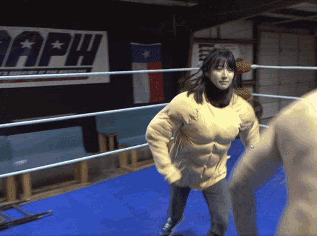 a woman in a muscle suit is in a boxing ring with a sign that says aph