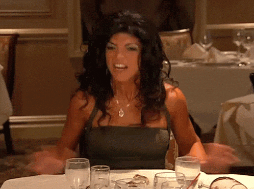 a woman in a black dress is sitting at a table with wine glasses