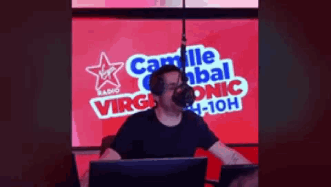 a man is talking into a microphone in front of a virgin radio sign