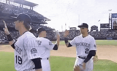 three baseball players are high fiving each other on the field .
