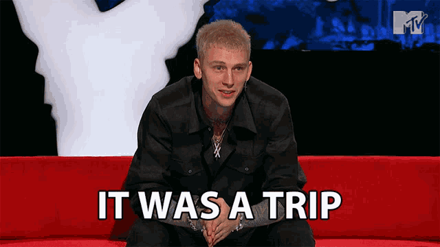 a man sits on a red couch with the words " it was a trip " behind him